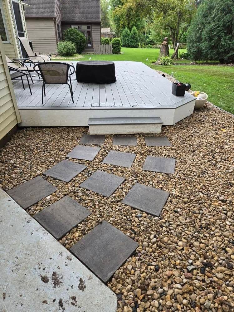 Stone pathway leading to a wooden deck in a landscaped backyard with greenery.