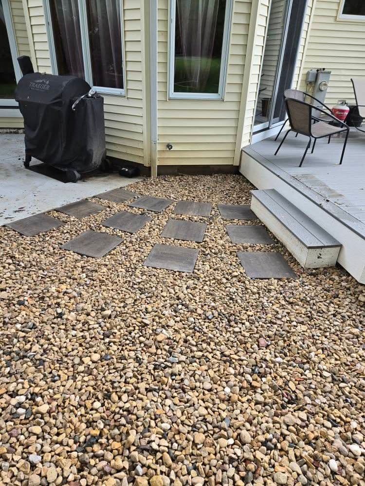Patio area with gravel, stepping stones, and a charcoal grill near a house.